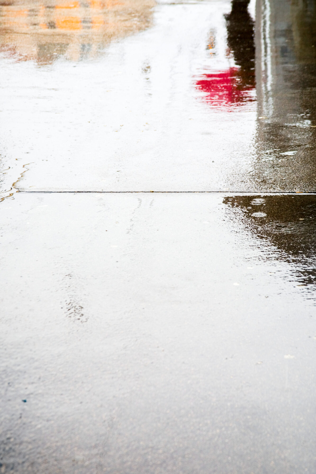 Spiegelung im Regen auf Straße mit rosa Regenschirm und orangenem Haus